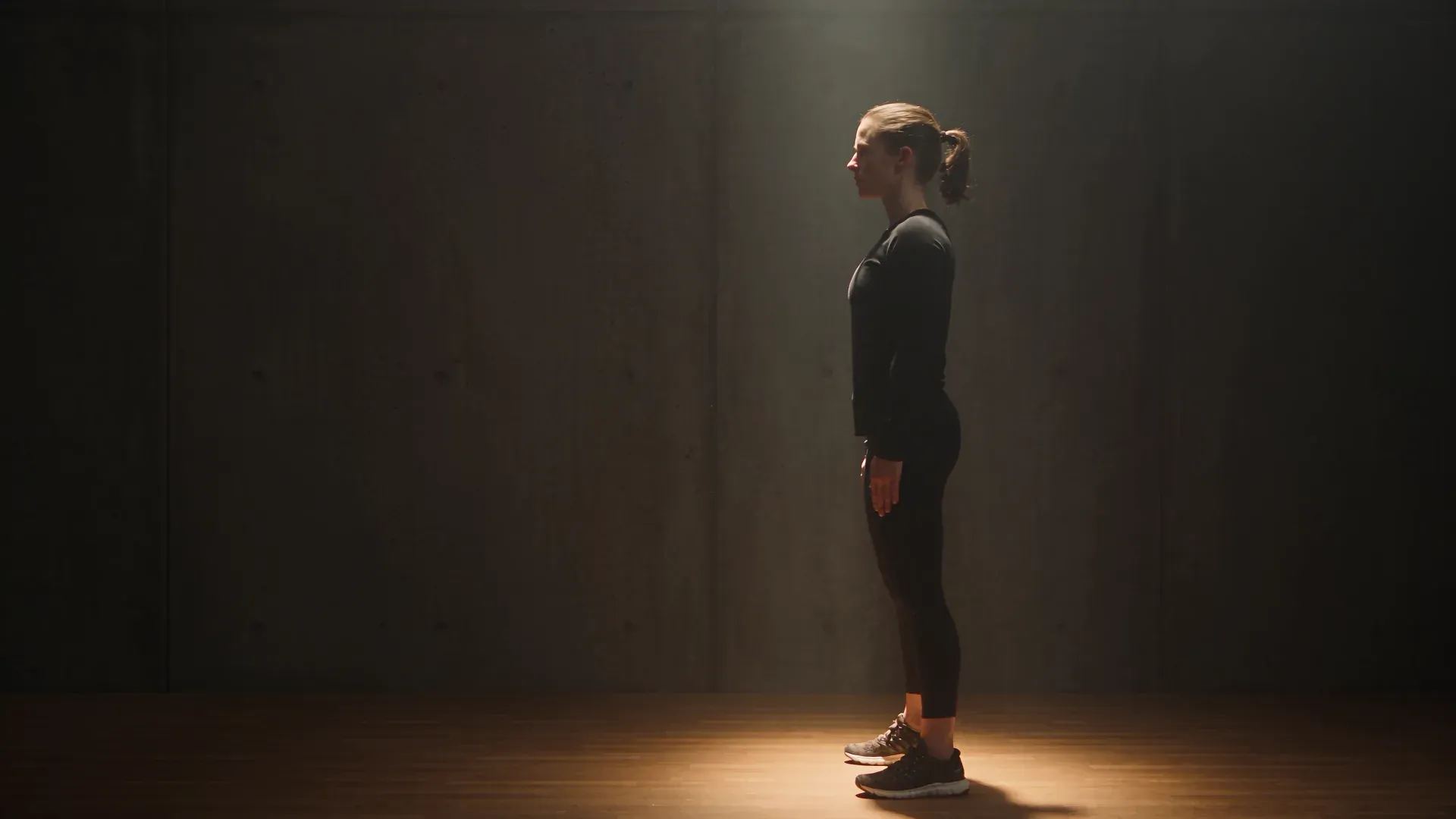 Sportistkinja izvodi pravilan čučanj pod reflektorom